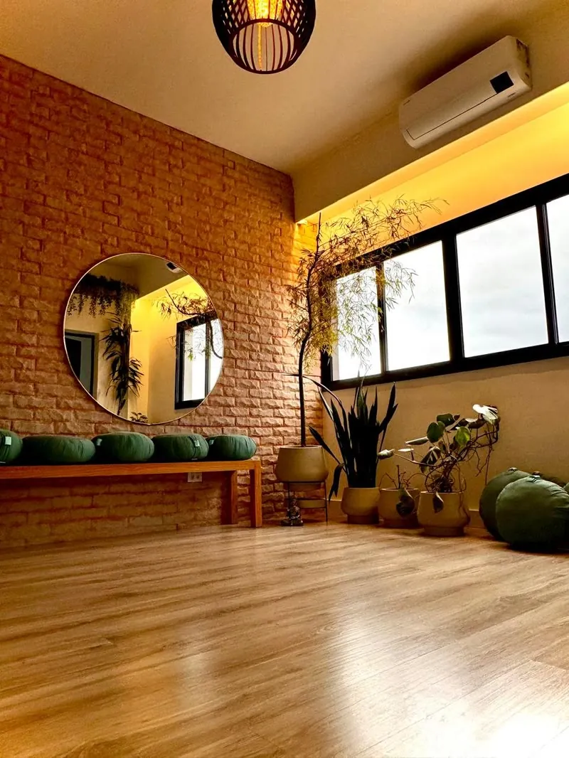 Sala de práticas com espelho redondo, banco de almofadas de meditação e plantas